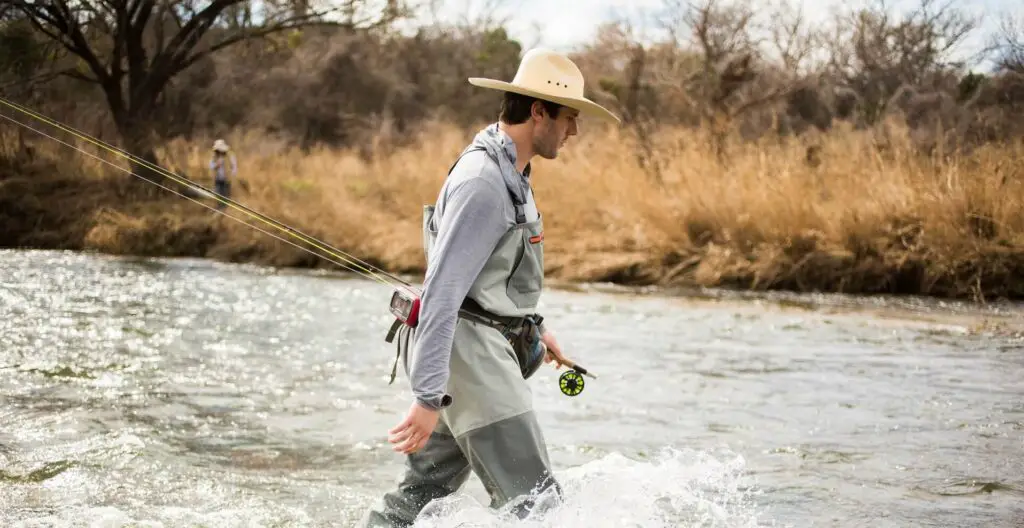 fly fisherman walking in river with hat
