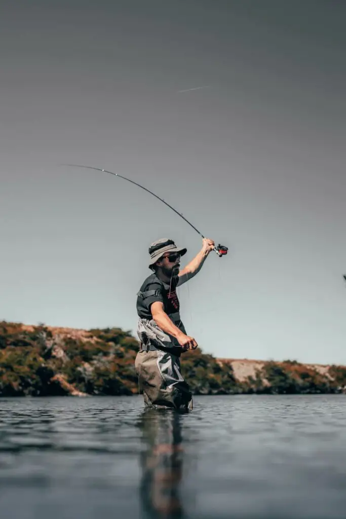 fly fisherman casting in river wearing a fly fishing hat