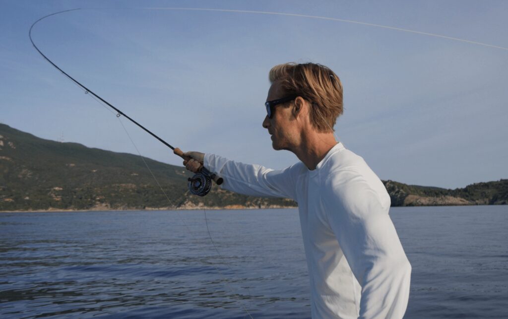 Fly fisherman casting a rod wearing a longsleeve fly fishing shirt
