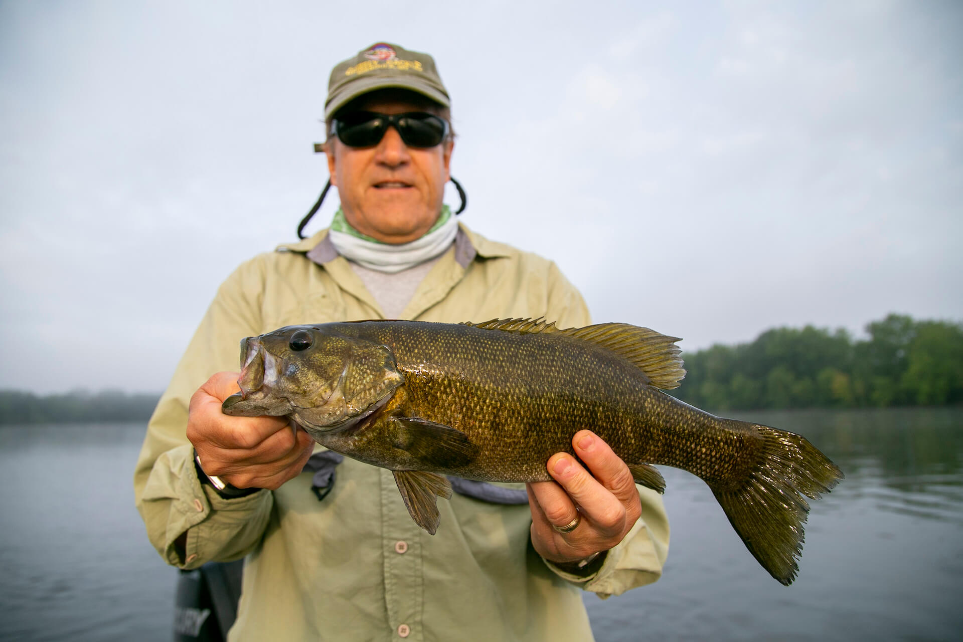 Black bass in the hands of a fisherman wearing a fishing shirt