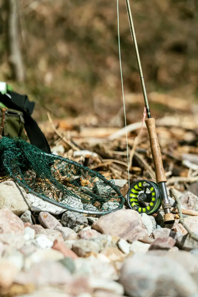 Fly rod and fly fishing net on rocky beach