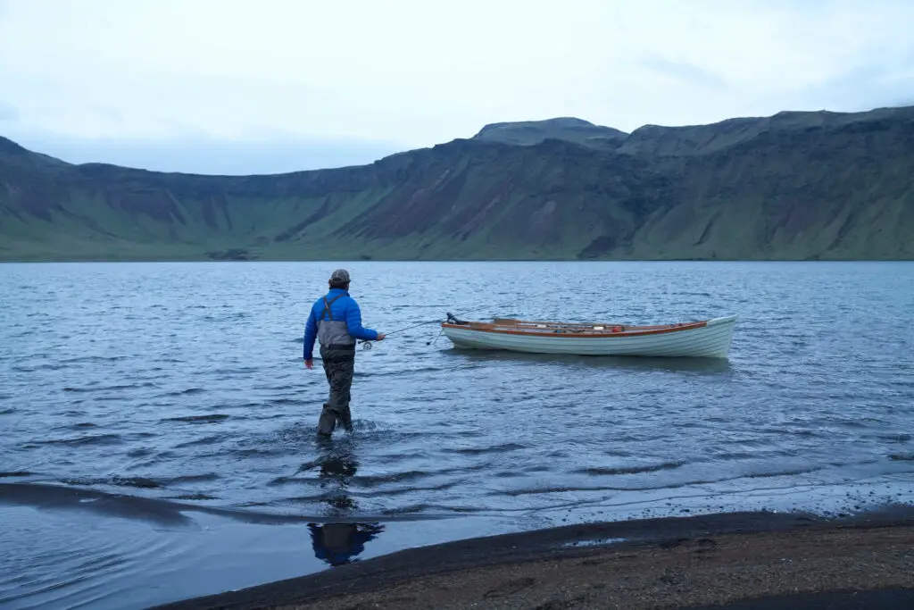 Fly fisherman walking to a boat with a rod in hand 