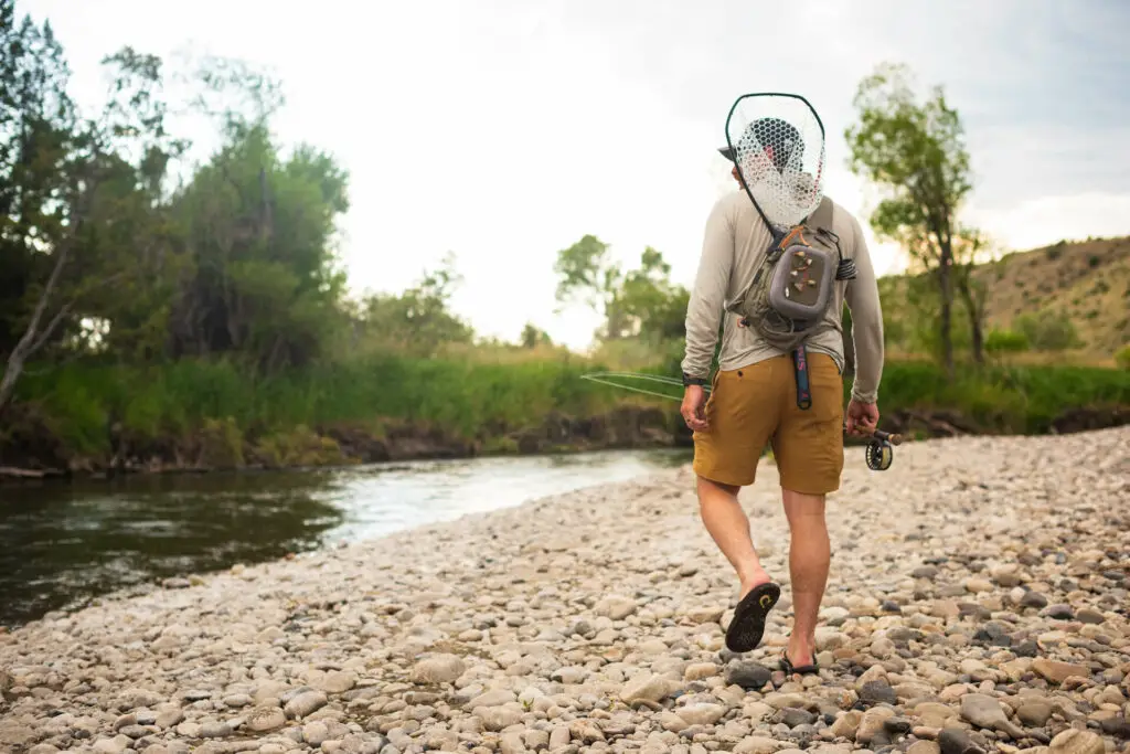 Fly Fisherman carrying a landing net on the back walking towards a river