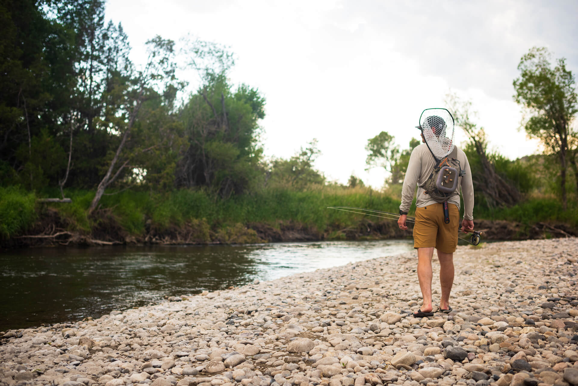 Fly fisherman walking along a river bank: wet wading for beginners guide