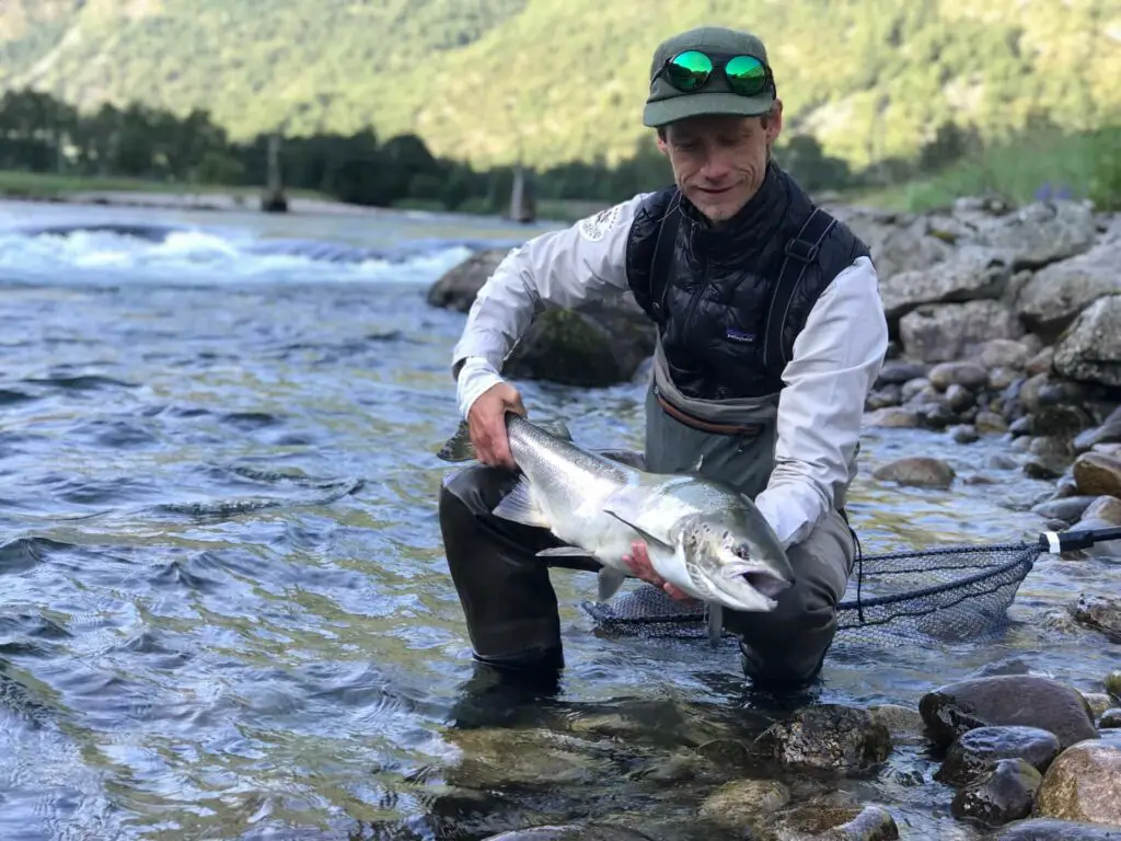 Fly fisherman with salmon in hand wearing the Oakley Clifden Polarized Fishing Sunglasses