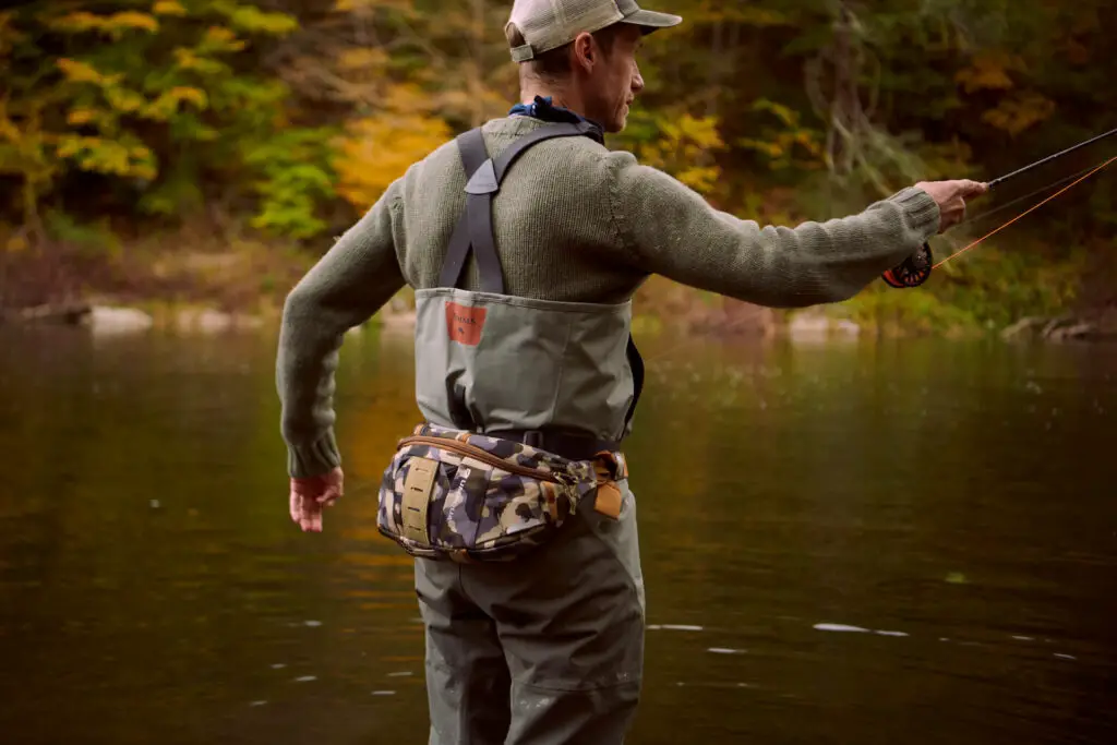 Fly fisherman casting a fly rod wearing the Bandolier sling pack