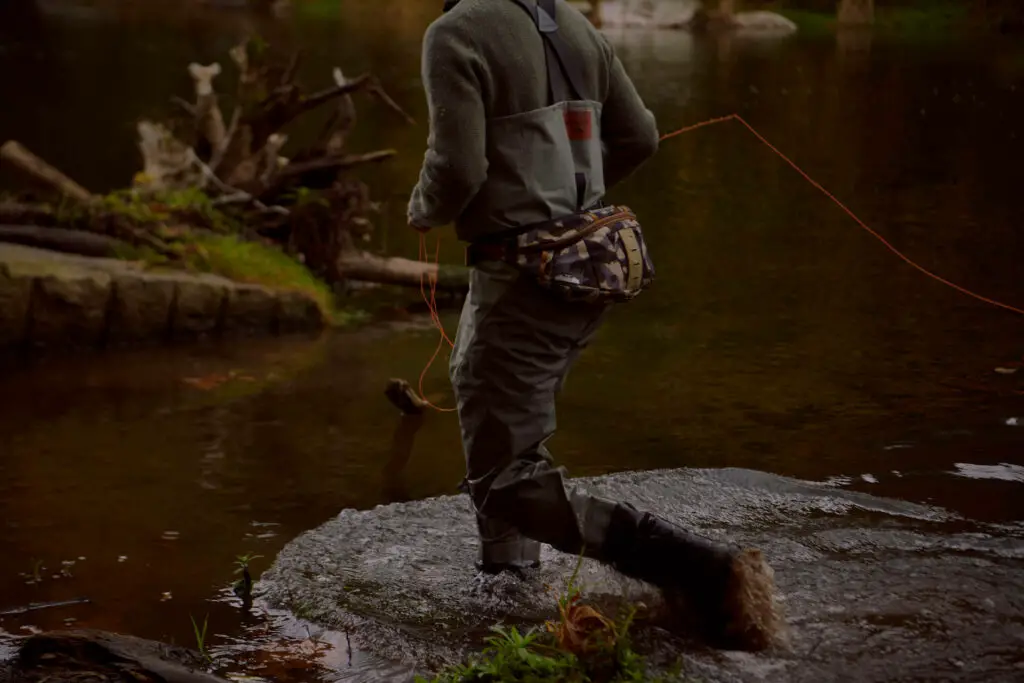 Fly fisherman wading in a river at dawn
