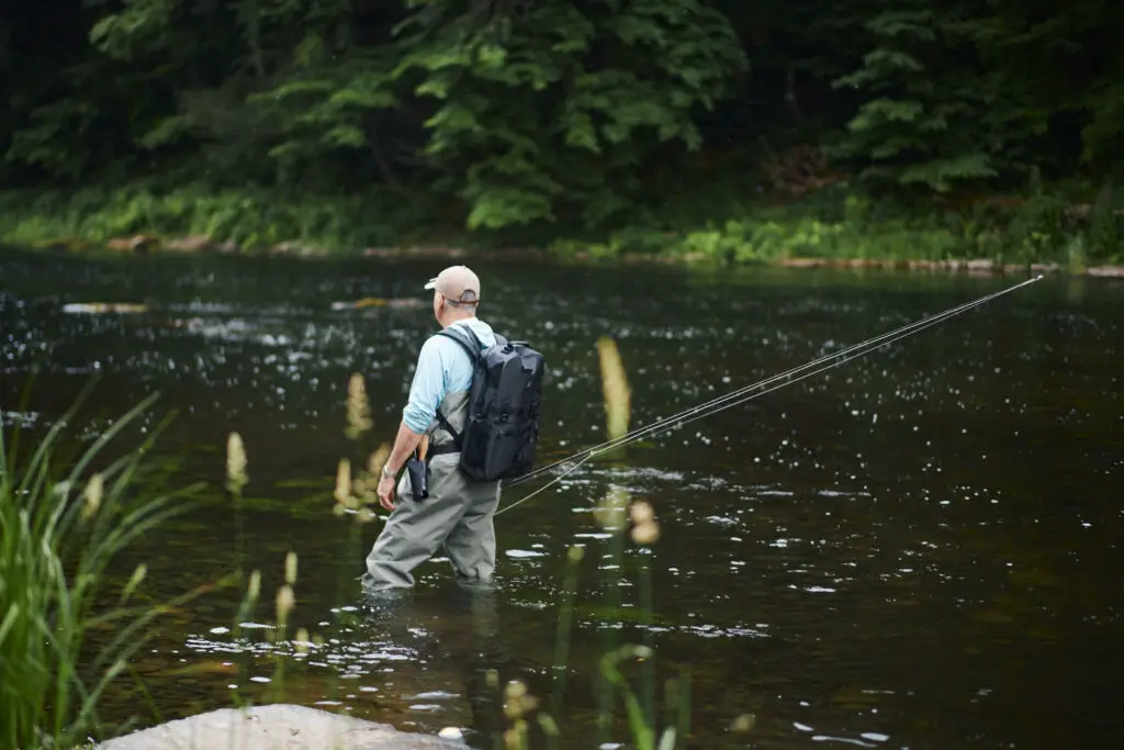 Fly fisherman standing in river with rod in hand and wearing the Breakwater Supply waterproof backpack